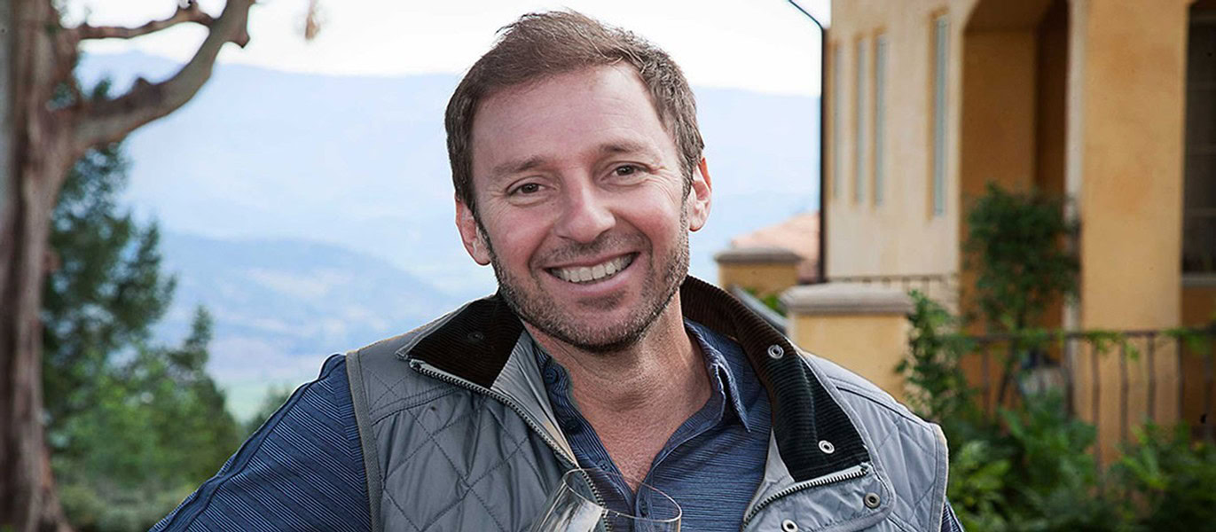Smiling winemaker outdoors at vineyard with scenic background.